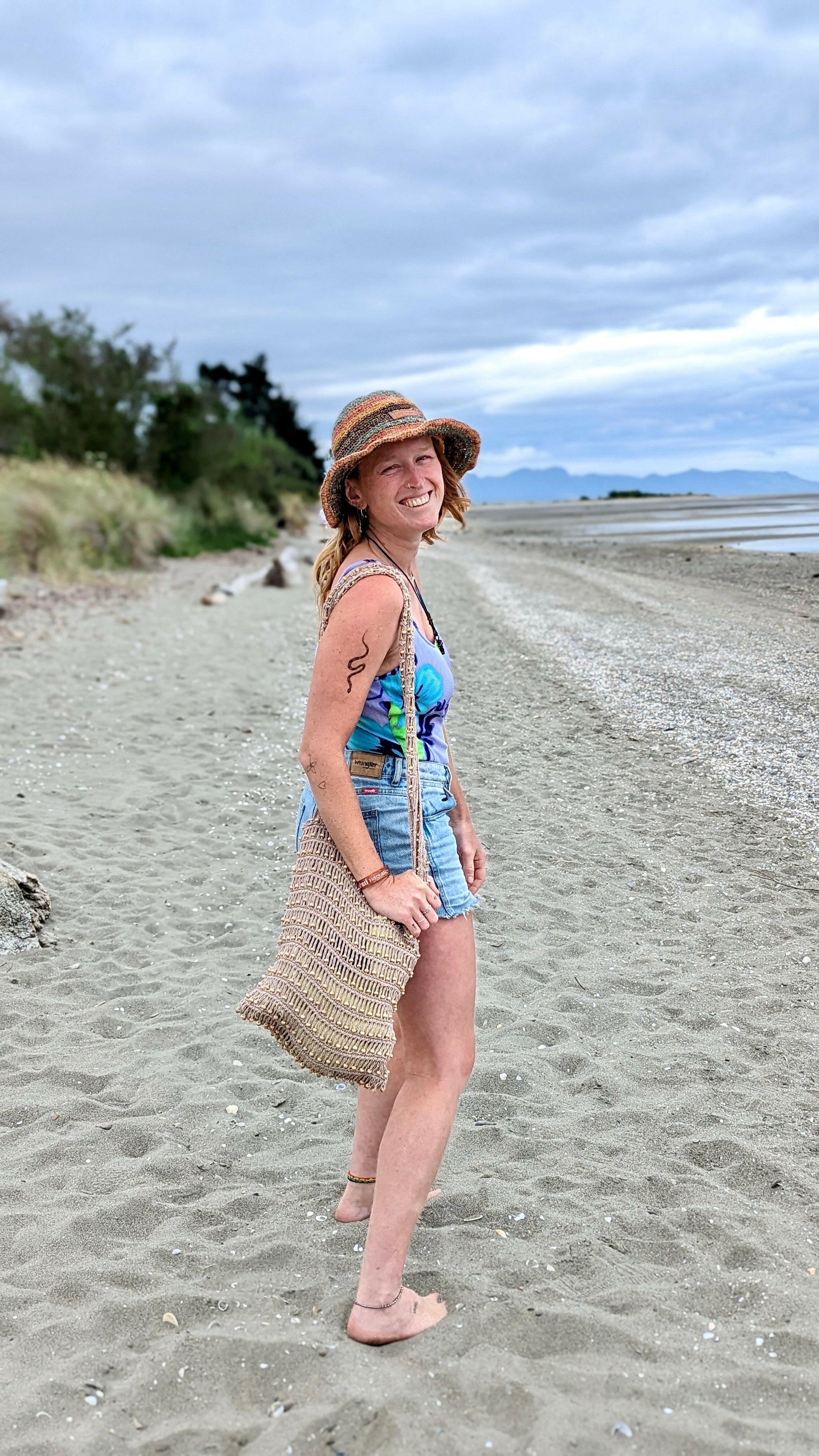 Girl smiling while wearing hemp hat and sustainable tote bag on beach in New Zealand
